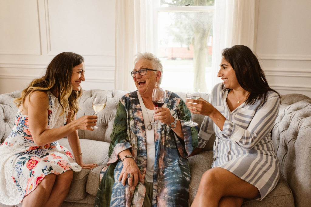 3 women sitting on sofa drinking Pelee Island Winery wine at The Leslie Style Vacation home in spring in Kingsville. 